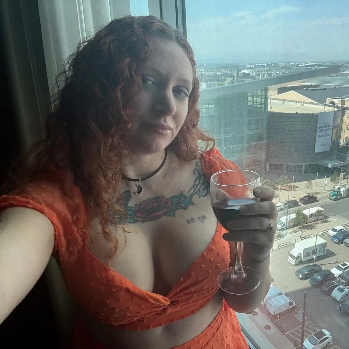 Maddy in an orange top beside a city-view window